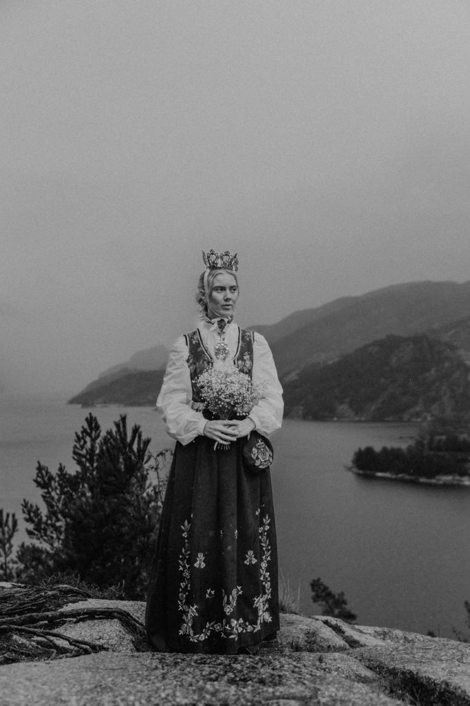 Bryllupsbilde av kvinne i tradisjonell norsk drakt med fjord og fjell i bakgrunnen.
