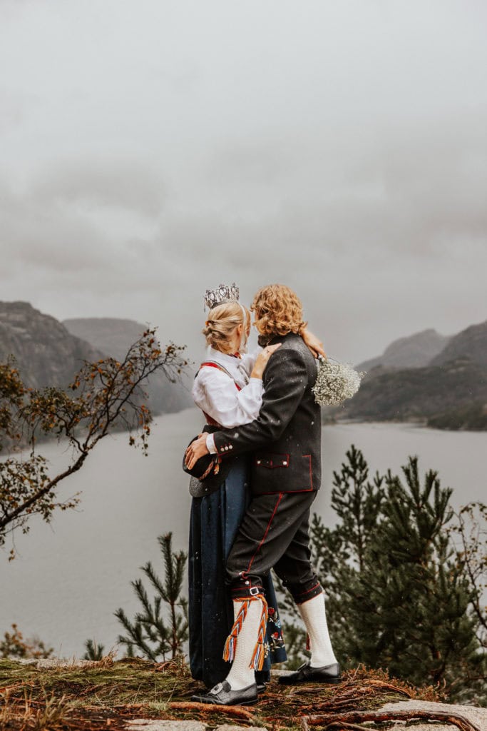 Bryllupsfoto av et par i tradisjonelle klær med fjell og fjord i bakgrunnen.