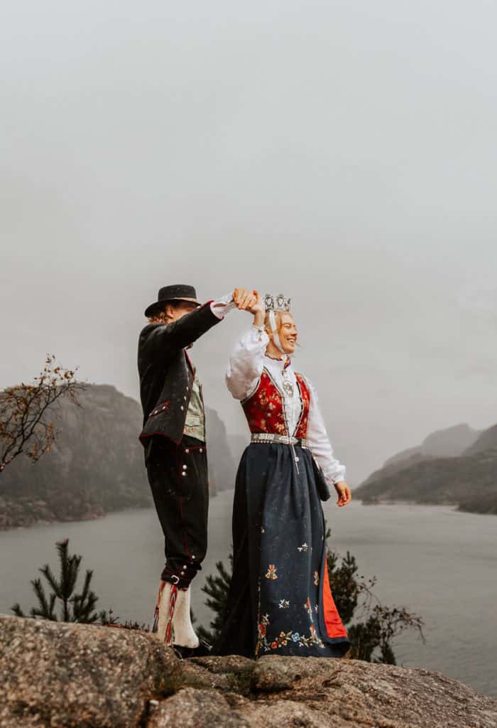 Vesle og kvinne i tradisjonell bunad holder hender ved Lysefjorden under bryllupsfotografering.