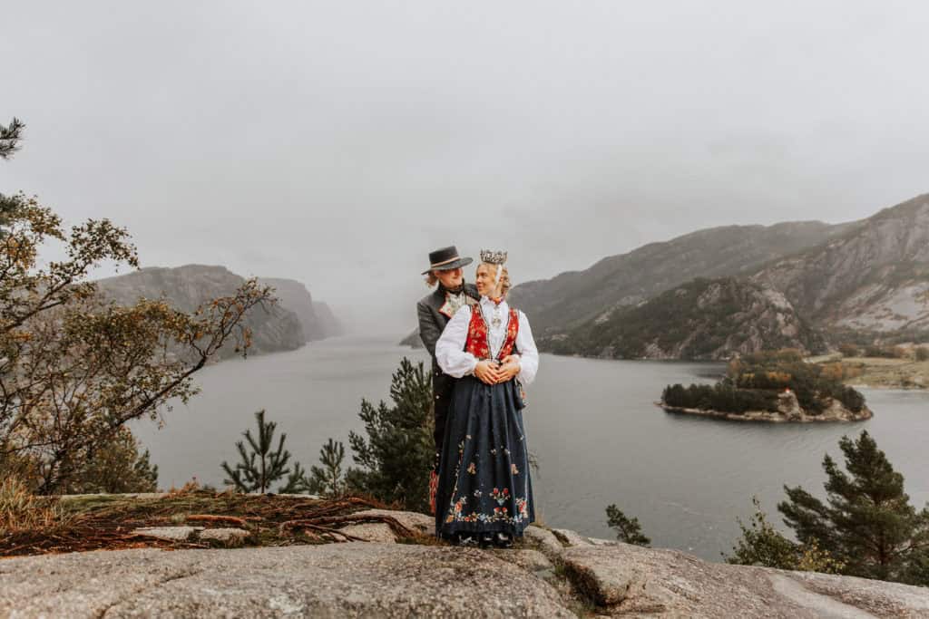 Vesle og mann i tradisjonelle klær ved Lysefjorden, omgitt av fjell og natur.
