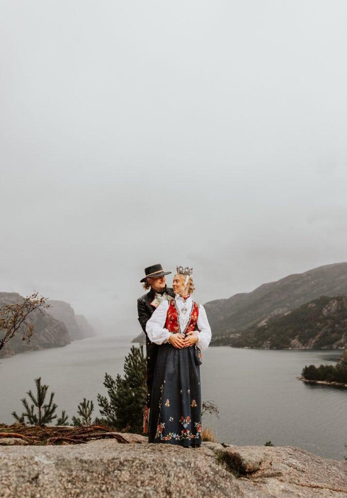Bryllupsfoto av et par i tradisjonelle klær med Lysefjorden i bakgrunnen.