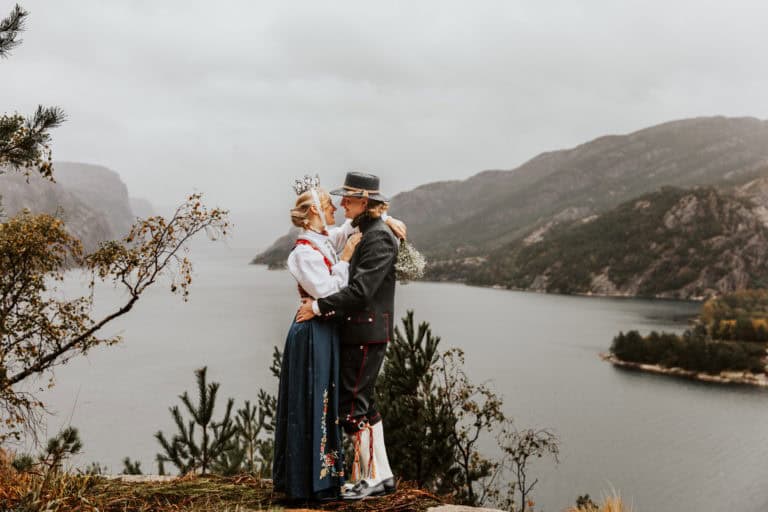 Bryllupsfoto av et par i tradisjonelle klær med Lysefjorden i bakgrunnen.