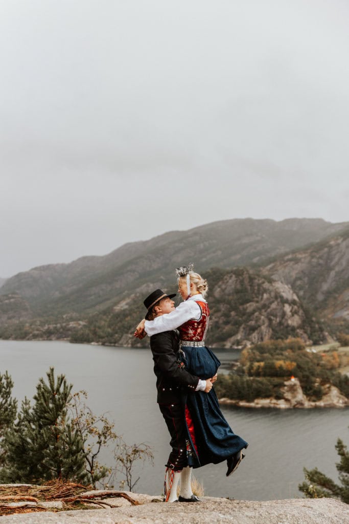 Bryllupsfoto med par i tradisjonelle klær mot Lysefjorden og fjelllandskapet.